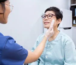 연하재활치료 장면. 치료사가 장갑을 낀 손으로 환자의 뺨을 짚어 삼킴 근육을 확인하고 있다
